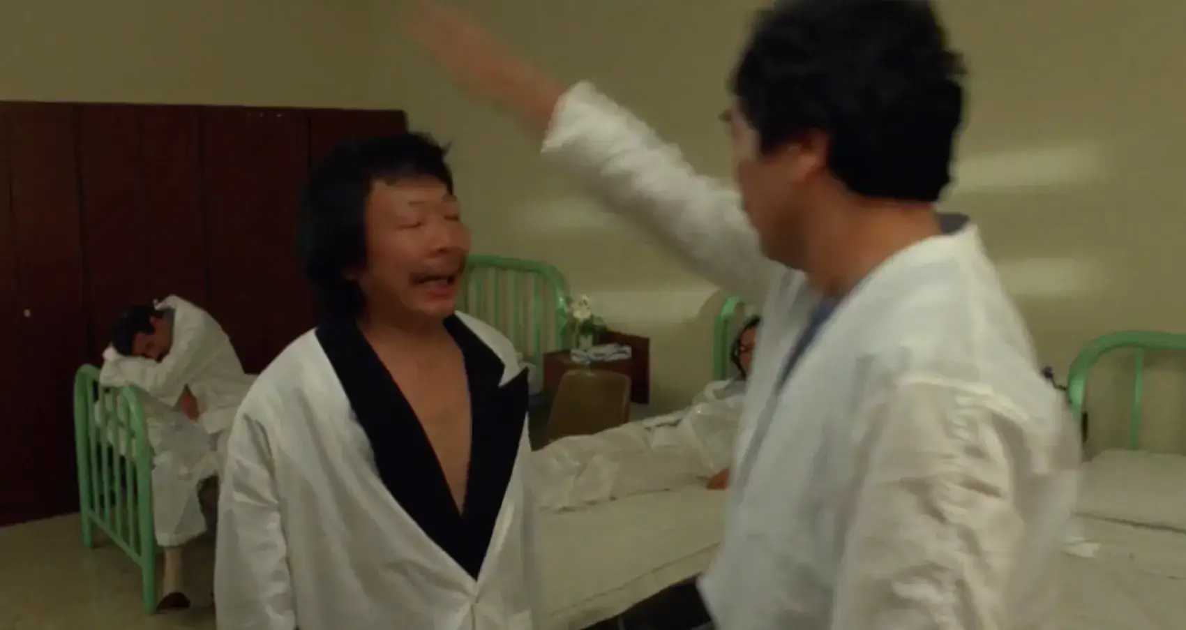 Image of Thoma's father in Wheels on Meals tapping the mental patient who thinks he's an alarm clock. The patient walks around the hospital wing making an alarm sound wobbling from side to side as alarm clocks do.